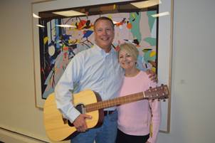 President and CEO Deb Archer (Greater Madison Convention & Visitors Bureau and Madison Area Sports Commission) stands with Jeff Holcomb Senior Convention Sales Manager at his celebration of 20 years of excellent work. Holcomb is holding a guitar, gifted to him by the organization, as Jeff a hobby musician has been known to use all of his skills—including his considerable songwriting talents to help groups.